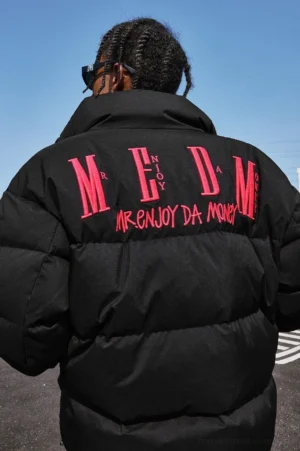 Rear view of a black oversized quilted puffer jacket with bold contrasting back lettering, stand collar, and relaxed Korean streetwear fit