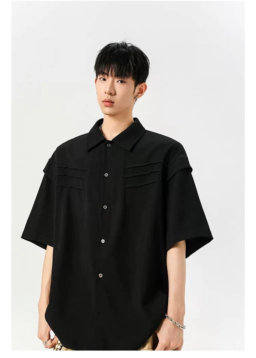 Black oversized short sleeve shirt close-up showing the front button closure, pointed collar, and pleated chest panels