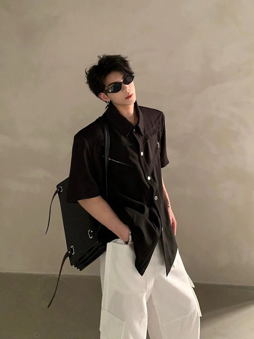 Side profile of black oversized short sleeve streetwear shirt with asymmetric hem, structured shoulders, pointed collar, and hand-in-pocket styling