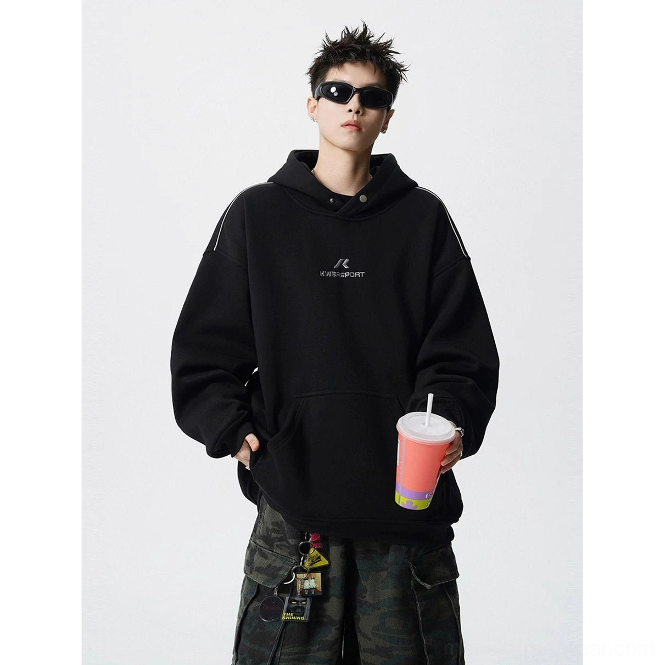 Black oversized streetwear hoodie with embroidered chest detail, ribbed cuffs and hem, and relaxed utility styling with camo cargo pants