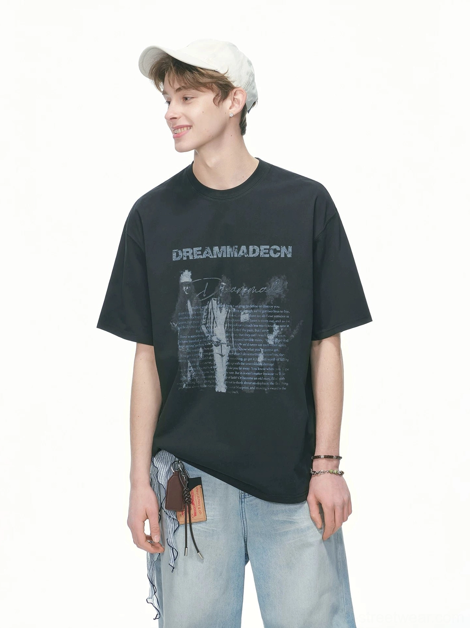 Black oversized streetwear T-shirt with faded vintage front artwork styled with wide leg jeans and white cap three quarter view