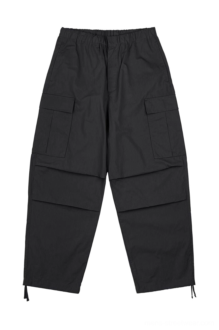 Black oversized utility cargo pants with elastic waistband flap pockets pleated knees and adjustable drawstring cuffs flat lay