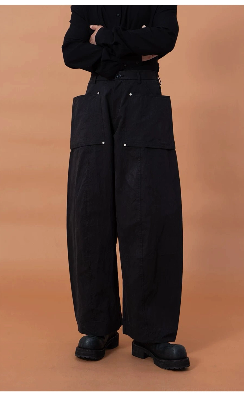 Black oversized utility cargo pod pants with large front pockets, metal rivet accents, and a sturdy wide-leg streetwear silhouette