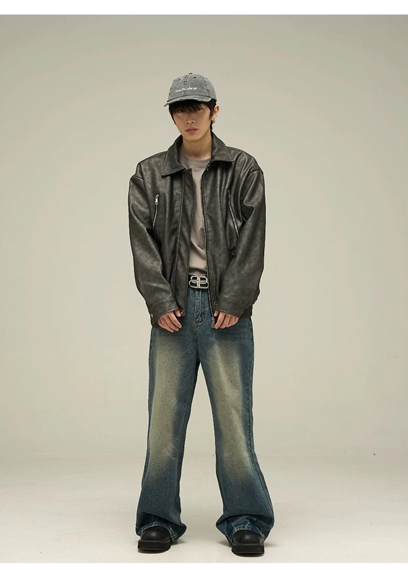Full body view of a black faded oversized faux leather streetwear jacket styled with a beige tee, wide leg blue jeans, cap, and urban casual accessories