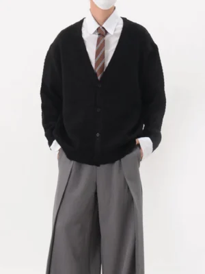 Black oversized waffle knit V-neck cardigan styled with white shirt striped tie and grey wide-leg trousers front view