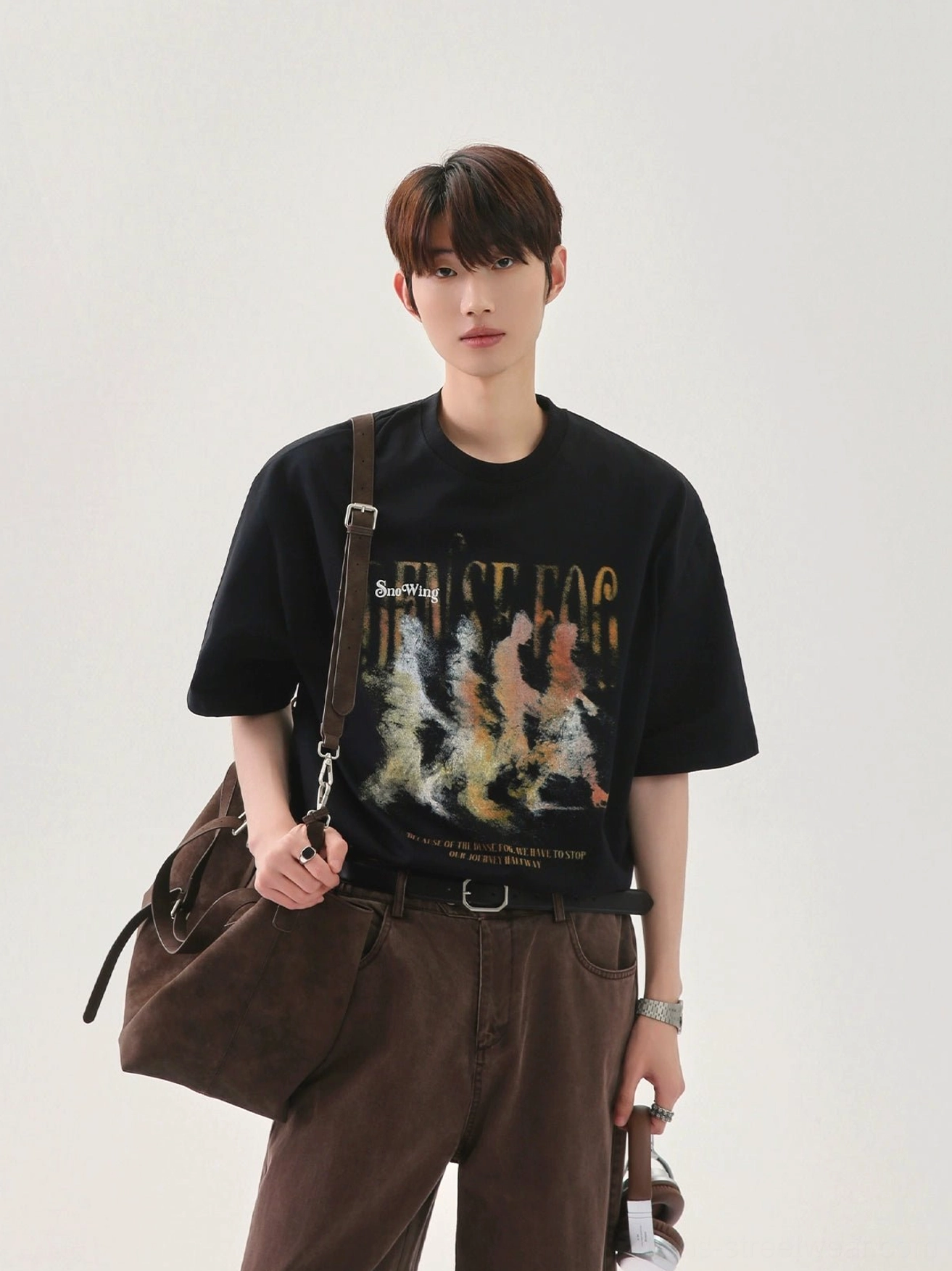 Black oversized graphic T-shirt with warm gradient marching figure artwork, relaxed fit, leather shoulder bag, and modern streetwear styling