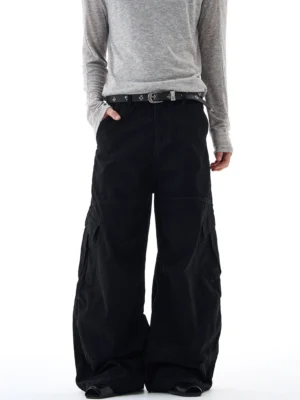 Black oversized wide-leg cargo pants shown from the front with matte cotton fabric, side utility pockets, and relaxed streetwear fit