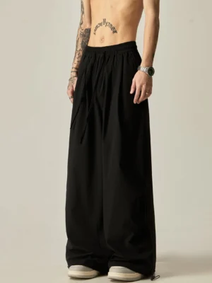 Black oversized wide leg drawstring pants for men shown from a low front angle with an elastic waist and adjustable ankle hems