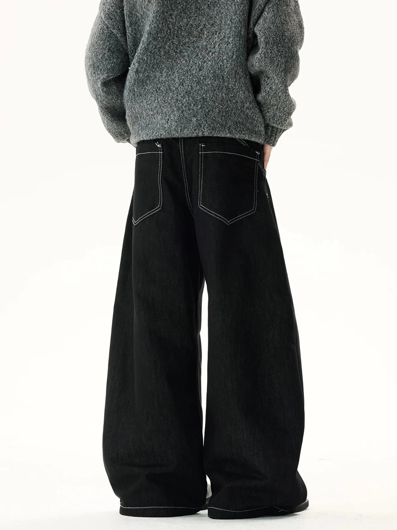 Rear view of black oversized wide-leg jeans with classic back pockets, contrast stitching, long draped legs, and minimalist avant-garde denim styling