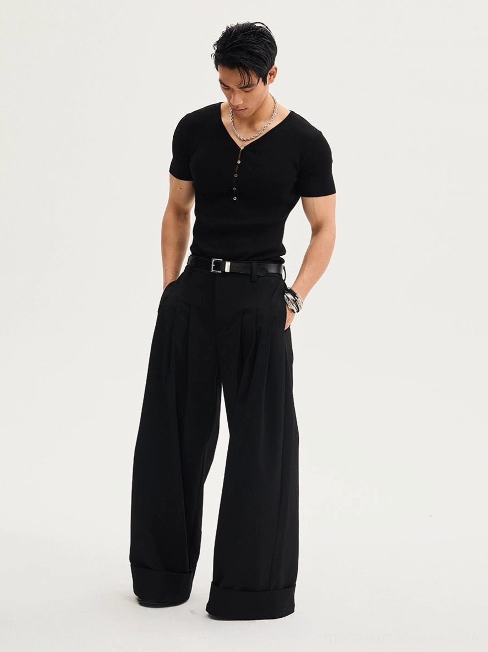 Black oversized wide-leg pleated trousers shown from a side-front view with hands in pockets, rolled cuffs, and relaxed Korean streetwear styling