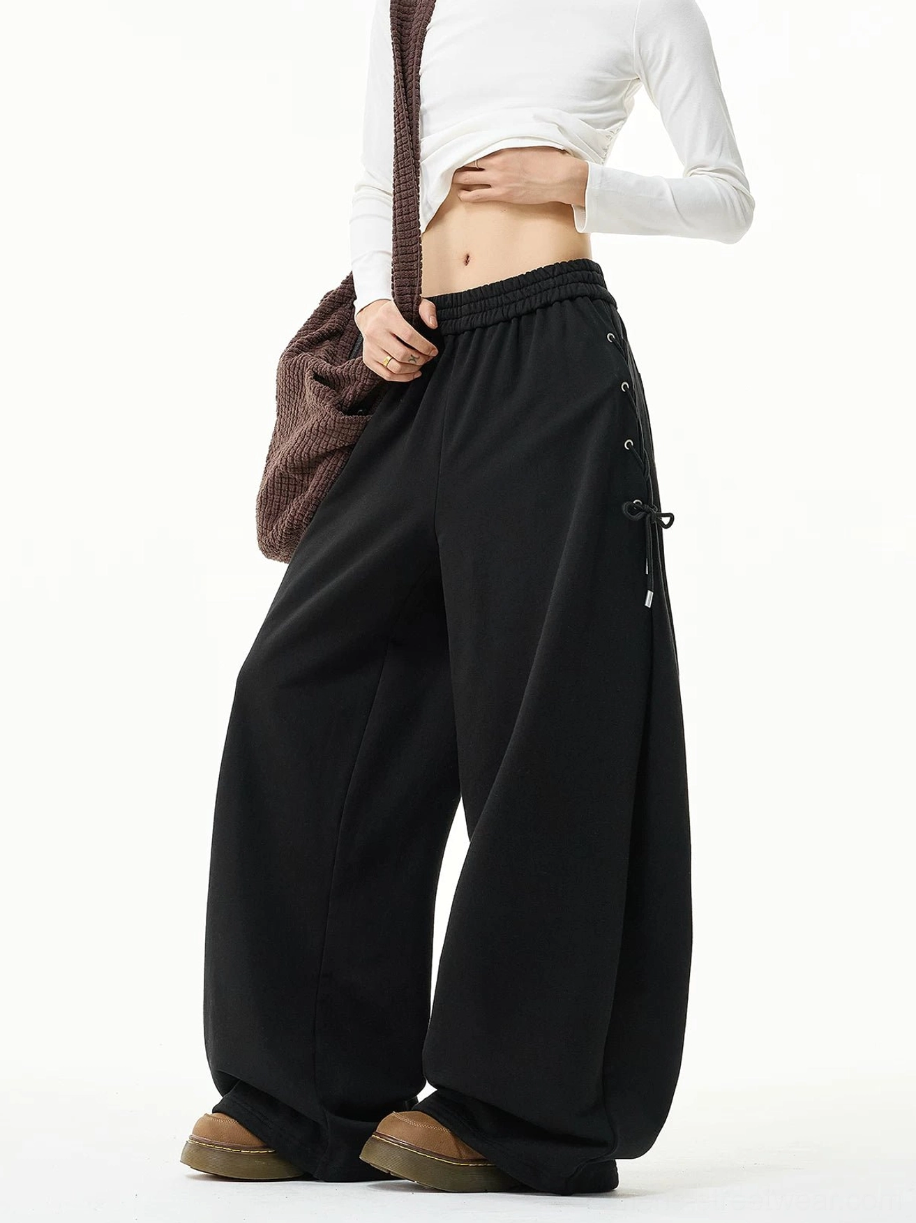 Black oversized wide-leg sweatpants with side lace-up detailing styled with a white cropped top and brown crossbody bag