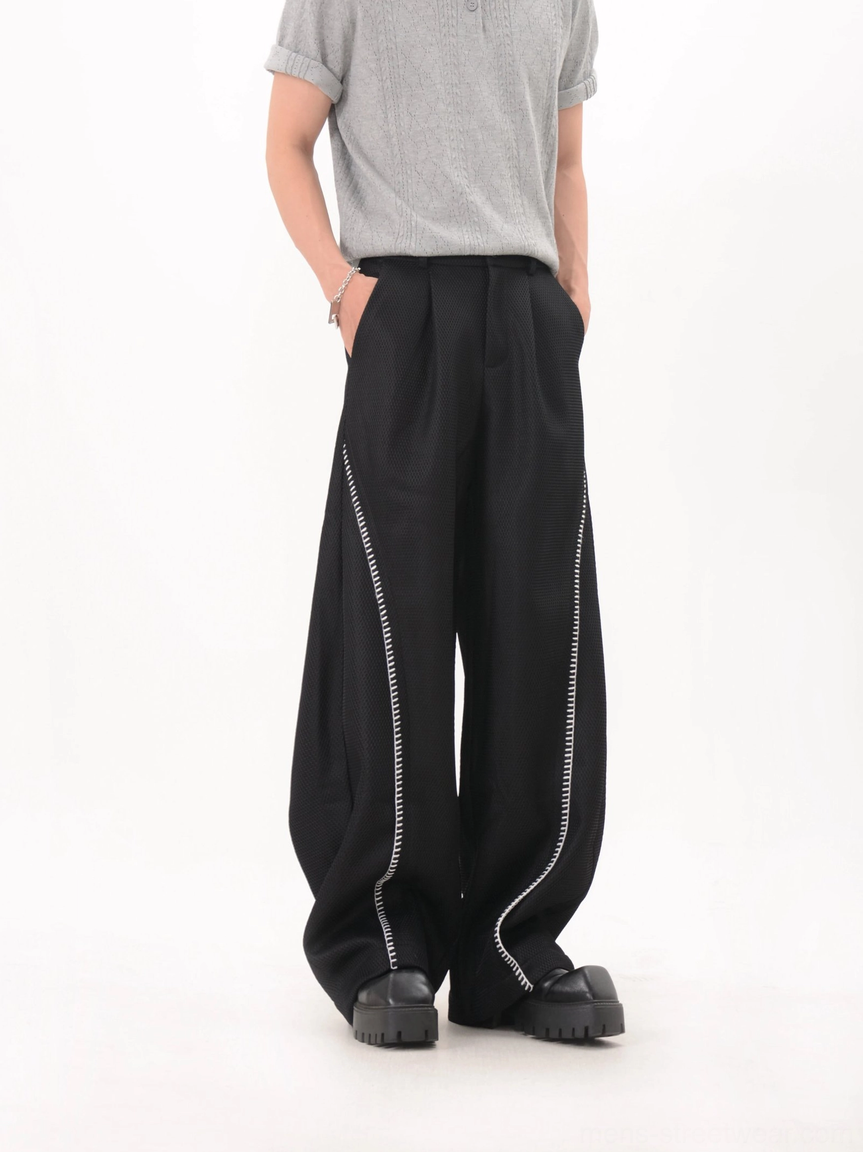 Black oversized wide leg trousers with white curved side piping and mesh inspired texture low angle view
