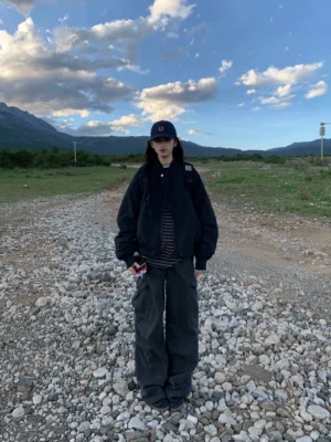 Black oversized zip-up bomber jacket full body front view with dark wide-leg cargo pants and mountain backdrop
