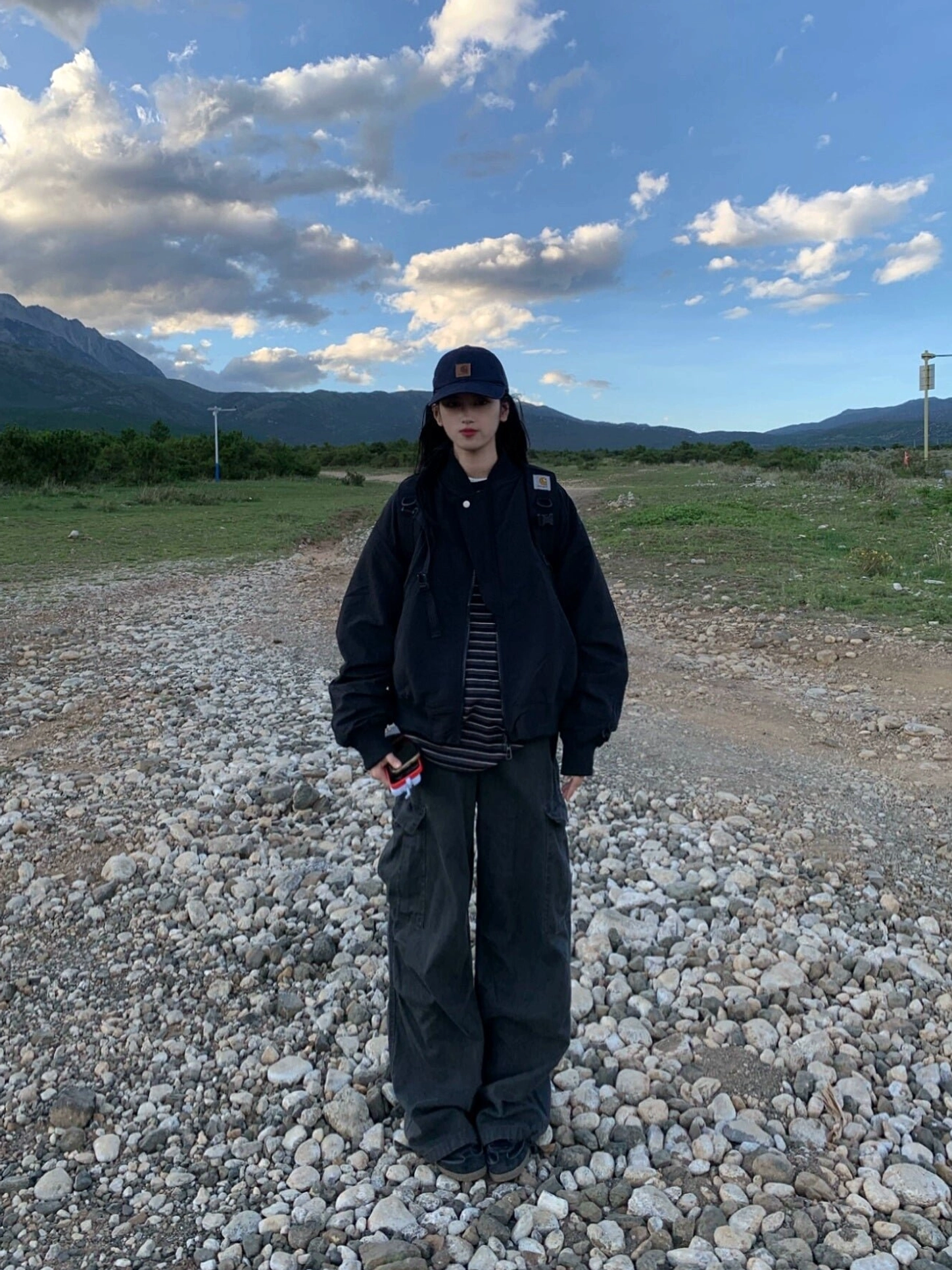 Black oversized zip-up bomber jacket full body front view with dark wide-leg cargo pants and mountain backdrop