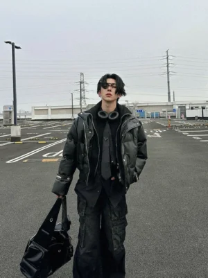 Full-body male streetwear look featuring a black padded faux leather puffer jacket with relaxed boxy fit, layered dark clothing, black duffel bag, and urban winter styling