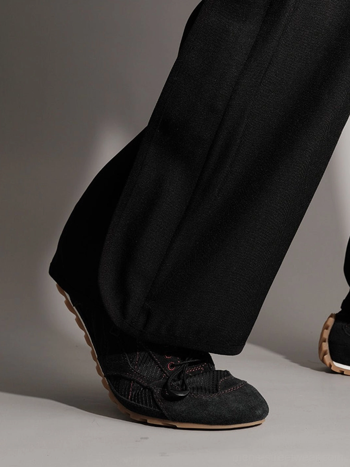 Black paneled low-profile trainers styled with wide-leg black trousers and visible tan rubber outsole