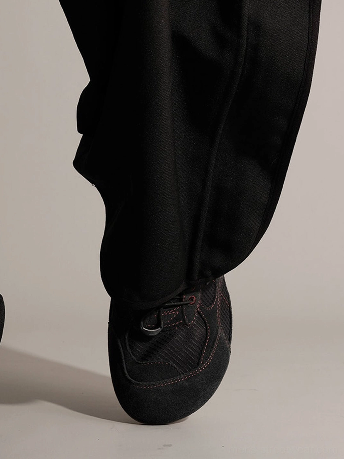 Black paneled nubuck trainers worn with wide-leg trousers showing rounded toe box and detailed upper stitching