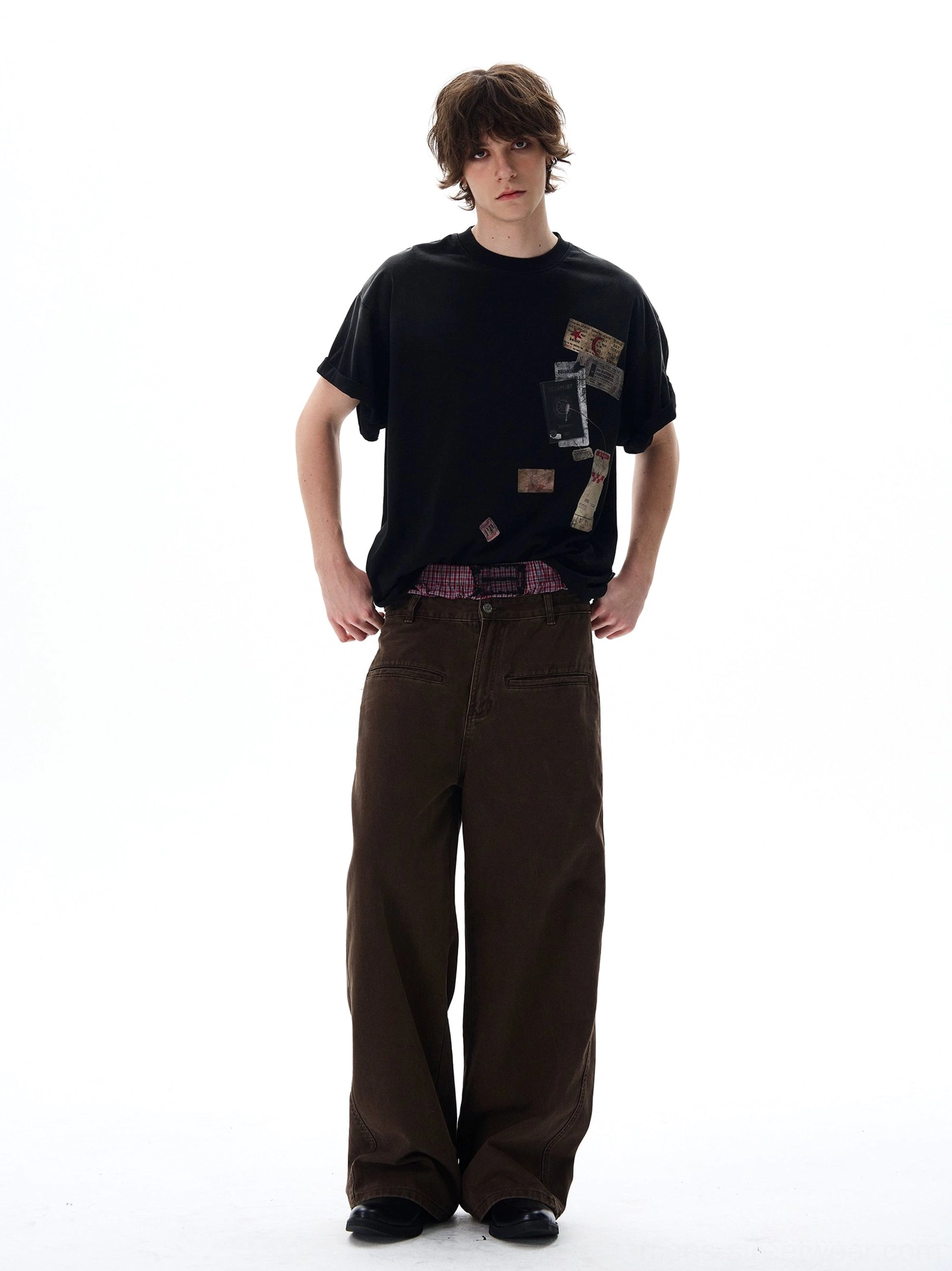 Black oversized graphic T-shirt with retro passport stamps and travel patch prints styled with brown wide-leg denim