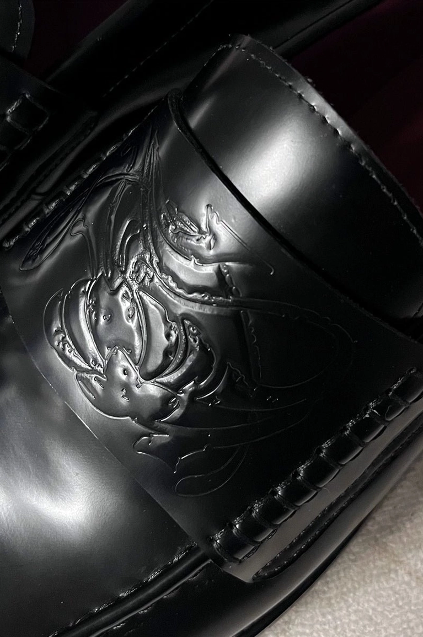 Close-up of embossed artwork and precise edge stitching on glossy black patent leather penny loafer vamp