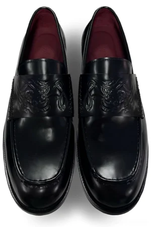 Top view of black embossed patent leather penny loafers with decorative vamp strap, rounded square toes, and low block heels