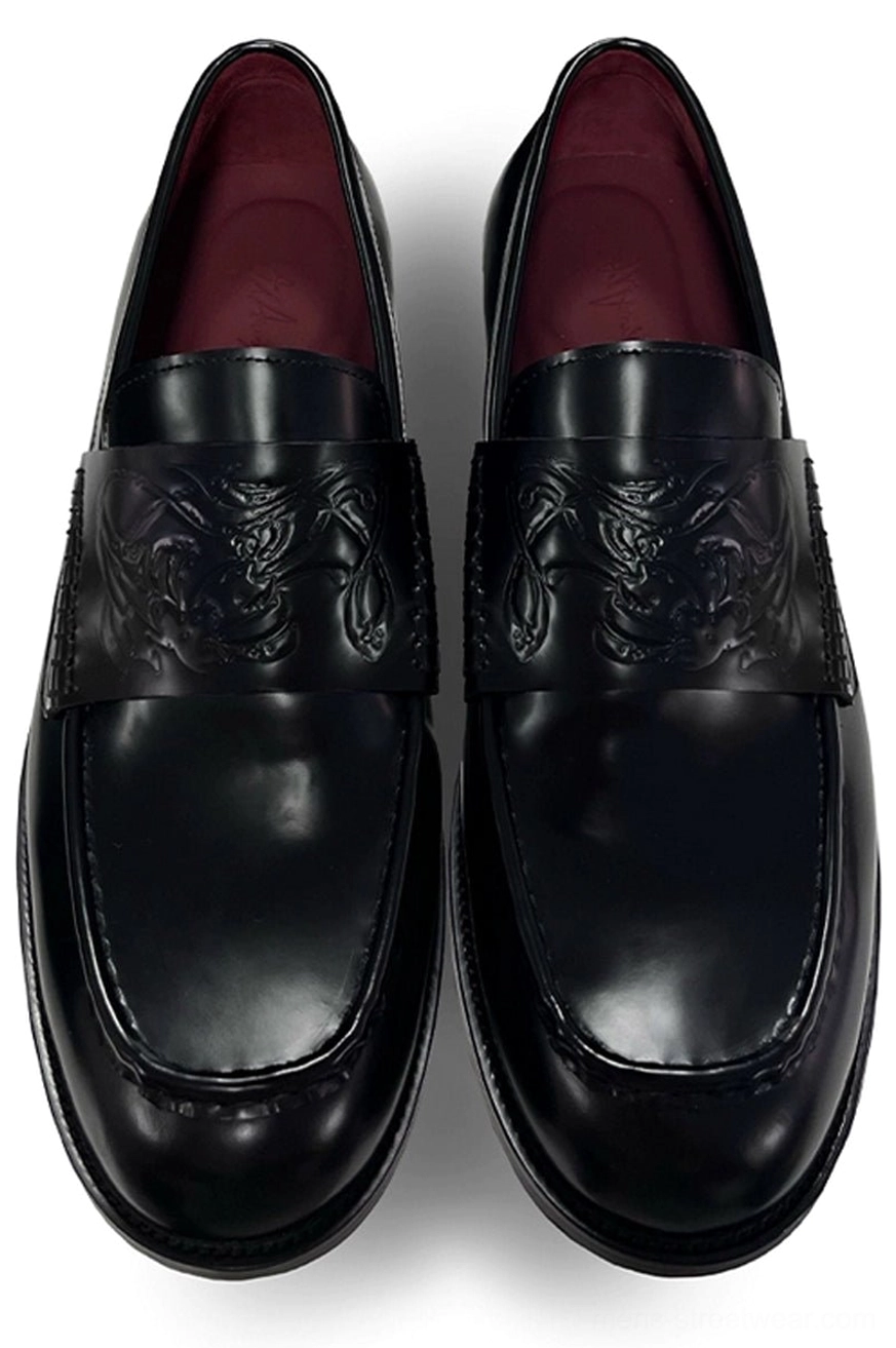 Top view of black embossed patent leather penny loafers with decorative vamp strap, rounded square toes, and low block heels