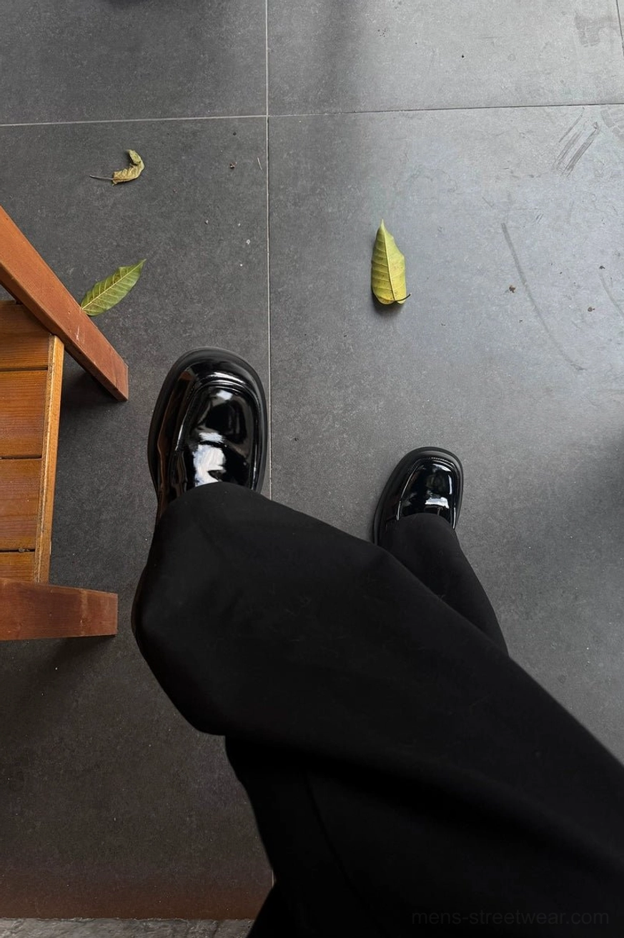 Black patent penny loafers styled with black formal trousers on an indoor tiled floor for a polished streetwear outfit