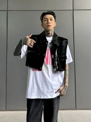 Front view of a black patent PU cropped utility vest styled over a white graphic T-shirt with wide-leg black jeans and chunky sneakers