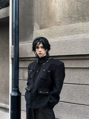 Black pearl-trimmed boucle jacket with boxy streetwear silhouette worn by a male model in a concrete city setting