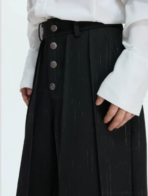 Black pinstripe high-waisted wide-leg suit trousers close-up showing pleated waist and decorative button details