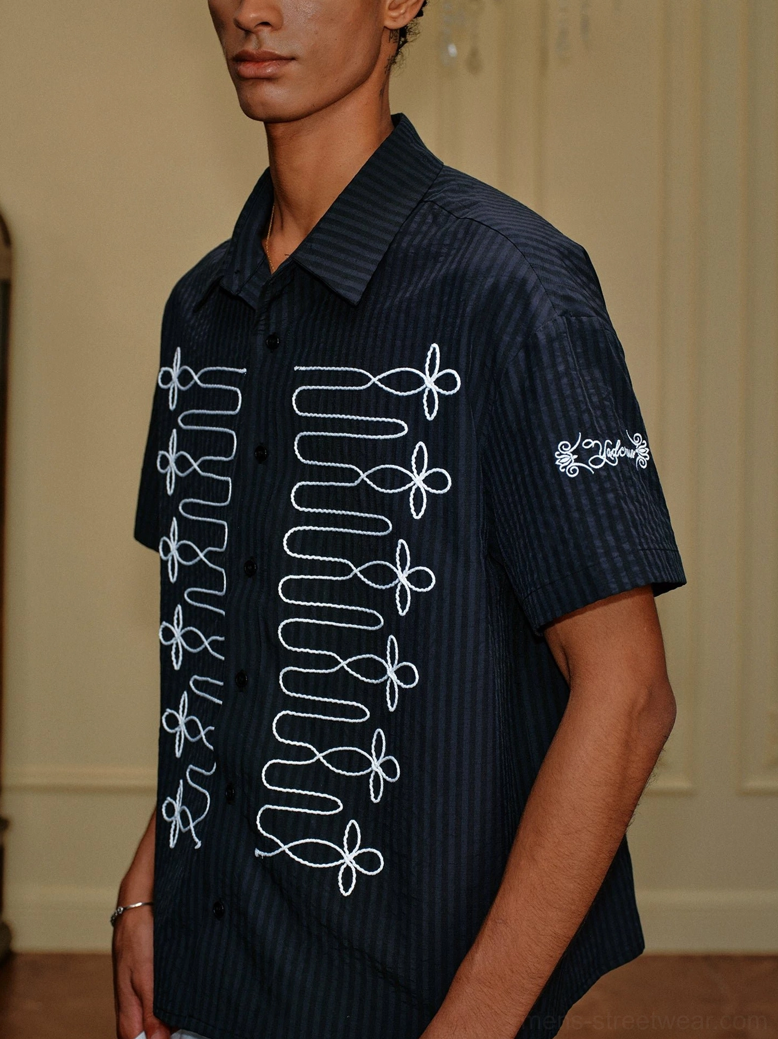 Side close-up showing black pinstripe short sleeve shirt with white loop embroidery, button collar, and sleeve detail
