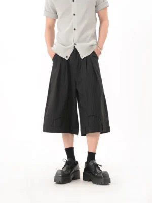 Front full-body view of black pinstripe pleated wide-leg cropped culotte pants styled with a grey knit shirt and black platform loafers