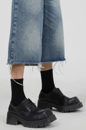 Model wearing black chunky platform Derby shoes with cropped frayed denim jeans and black crew socks in a streetwear outfit