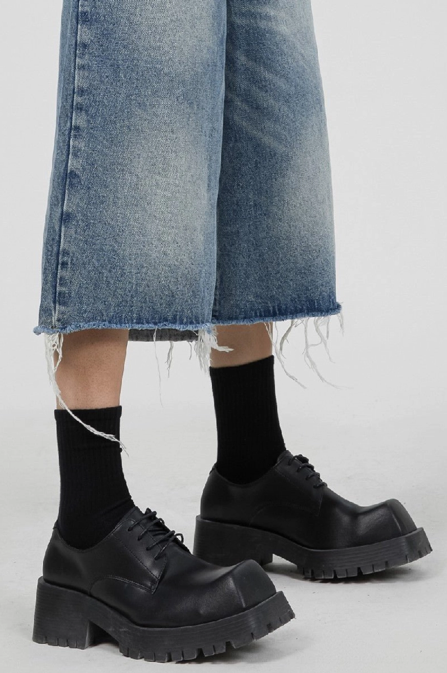 Model wearing black chunky platform Derby shoes with cropped frayed denim jeans and black crew socks in a streetwear outfit