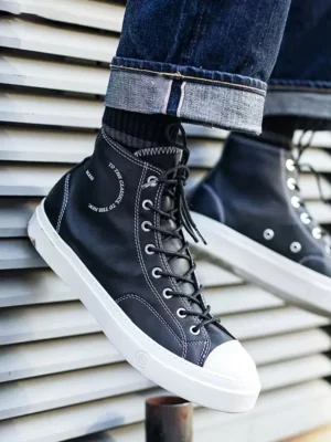 Black platform high-top streetwear sneaker worn with rolled dark denim jeans, featuring white contrast stitching and a clean rubber sole