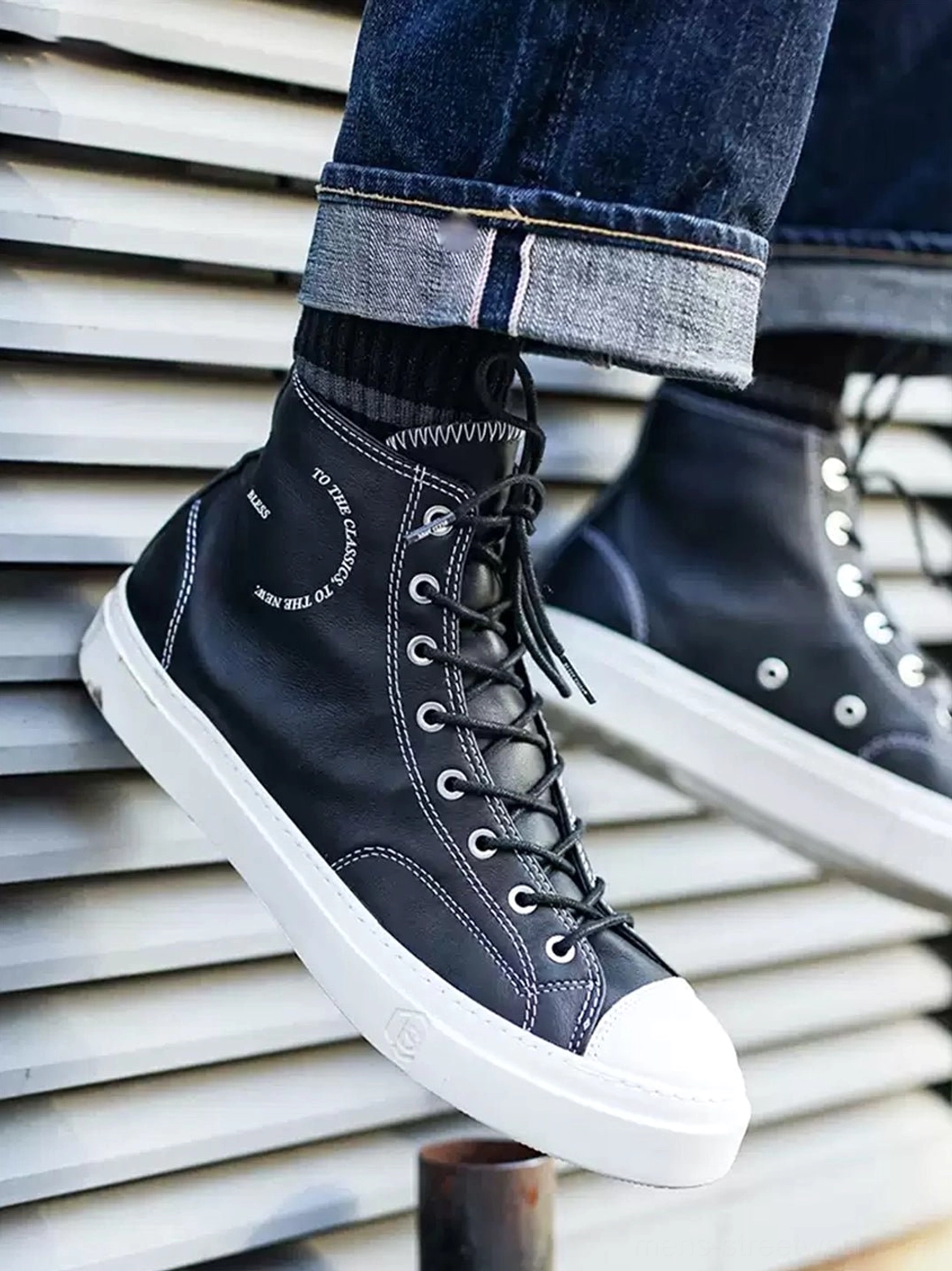 Black platform high-top streetwear sneaker worn with rolled dark denim jeans, featuring white contrast stitching and a clean rubber sole