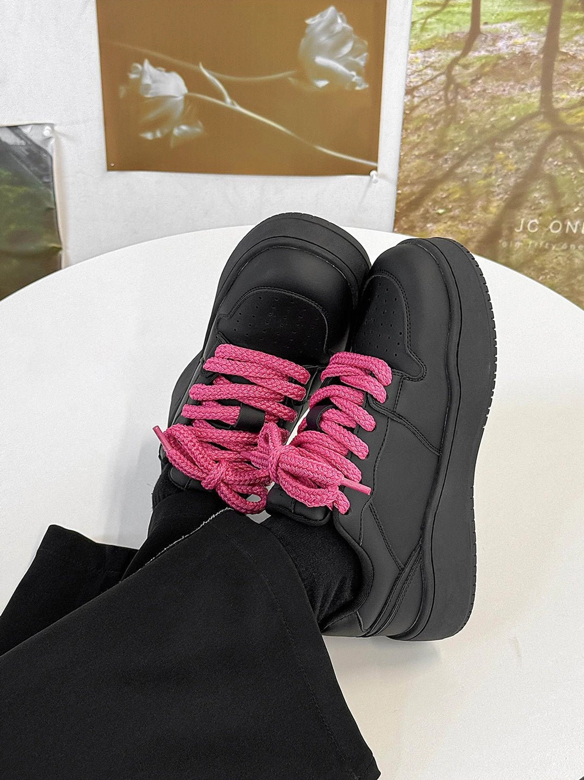 Top down view of black platform sneakers with hot pink laces worn with black trousers and socks