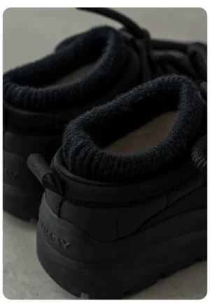 Close-up rear view of black platform sneakers showing the ribbed fleece collar, heel pull tab, structured heel counter, and urban trail-inspired design