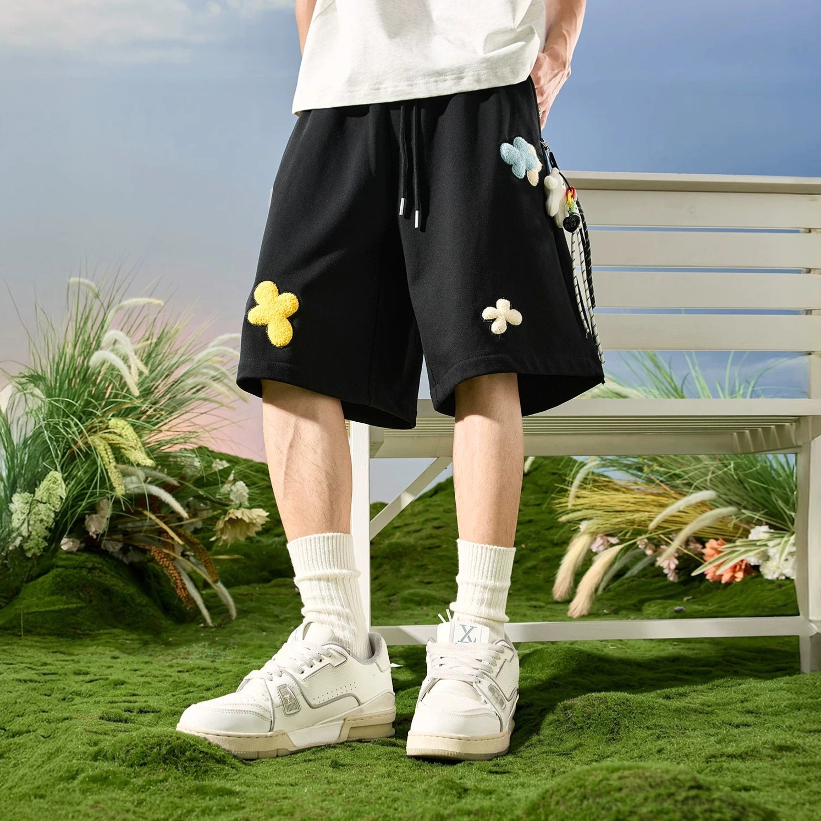 Black playful floral appliqué drawstring sweat shorts low-angle front view with textured flower patches
