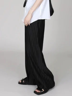 Black pleated floor-length wide-leg pants side view with flowing draped silhouette and black slide sandals