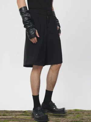 Black pleated tailored longline Bermuda shorts shown from the front side with zipper fly, wide tailored legs, and contemporary Seoul streetwear styling