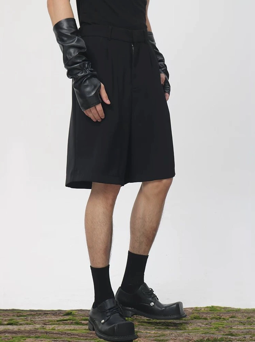 Black pleated tailored longline Bermuda shorts shown from the front side with zipper fly, wide tailored legs, and contemporary Seoul streetwear styling
