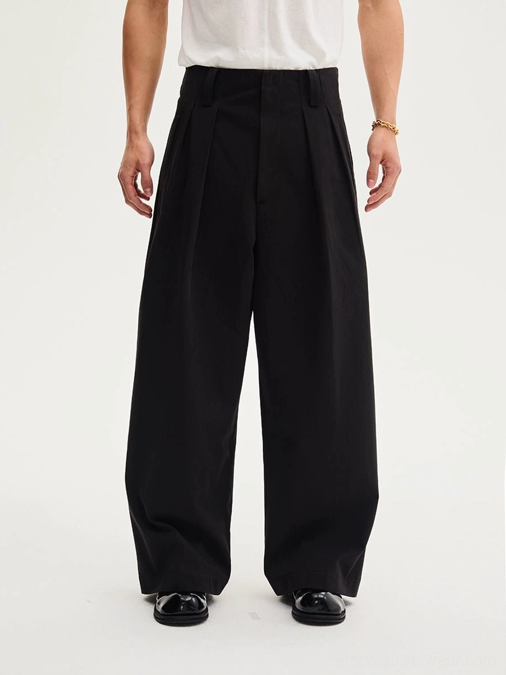 Lower-body close-up of black pleated tailored wide-leg trousers showing the high waist, structured fabric, and elongated leg silhouette