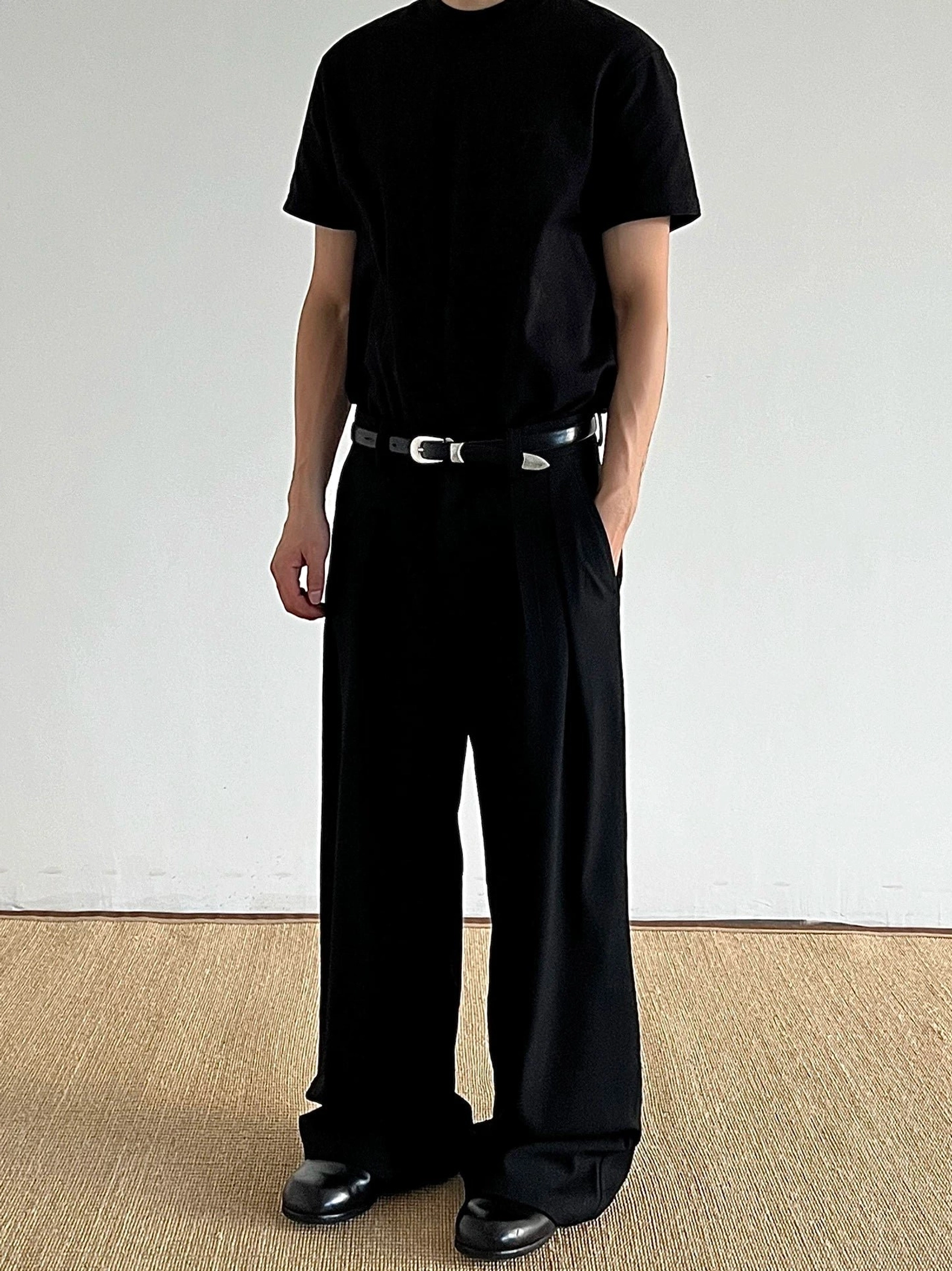 Black pleated wide-leg tailored trousers with full-length drape and leather shoes in a monochrome streetwear outfit