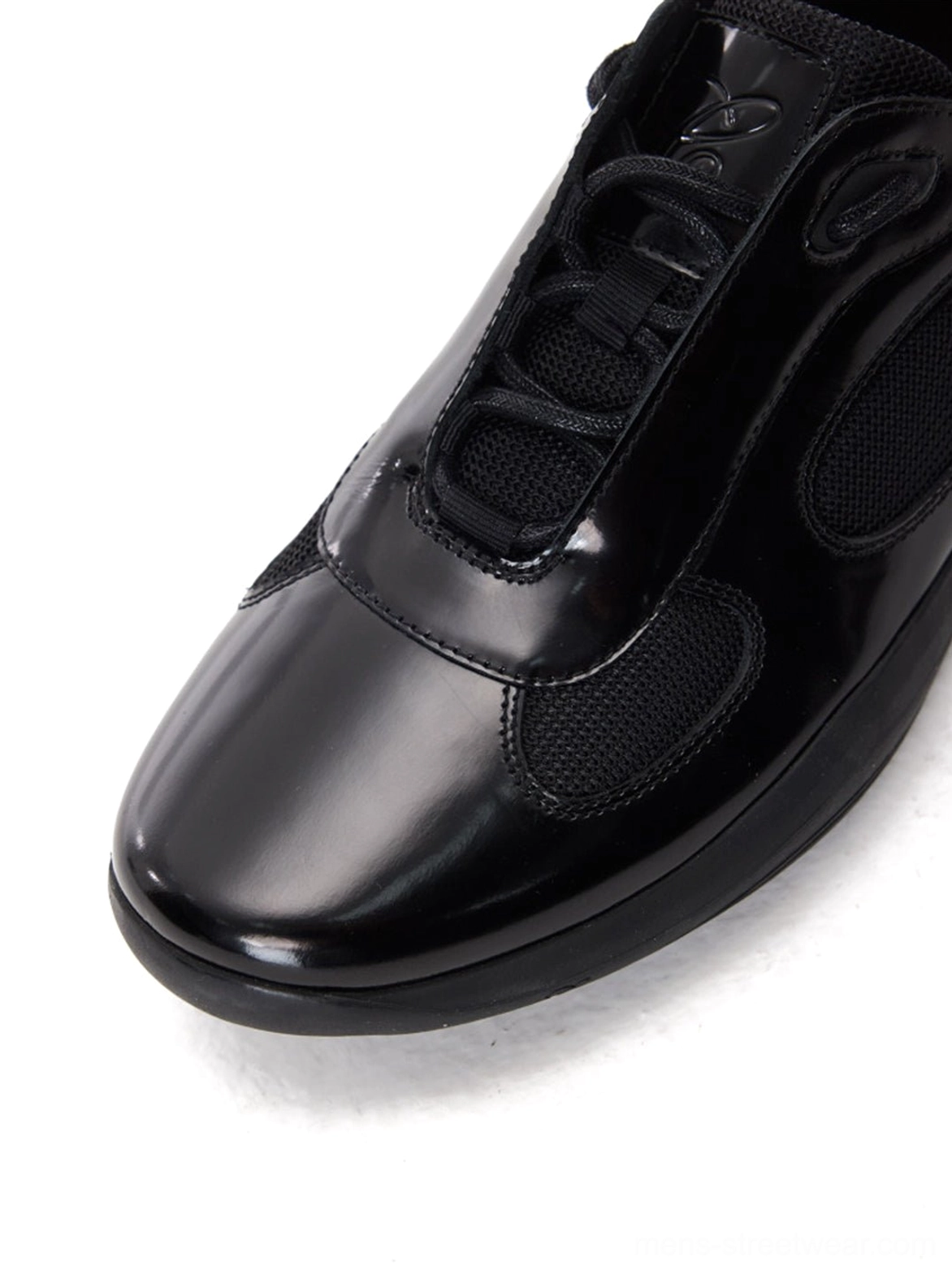 Front three-quarter close-up of black polished leather retro runner sneakers with rounded toe lace-up closure and ventilation mesh panels