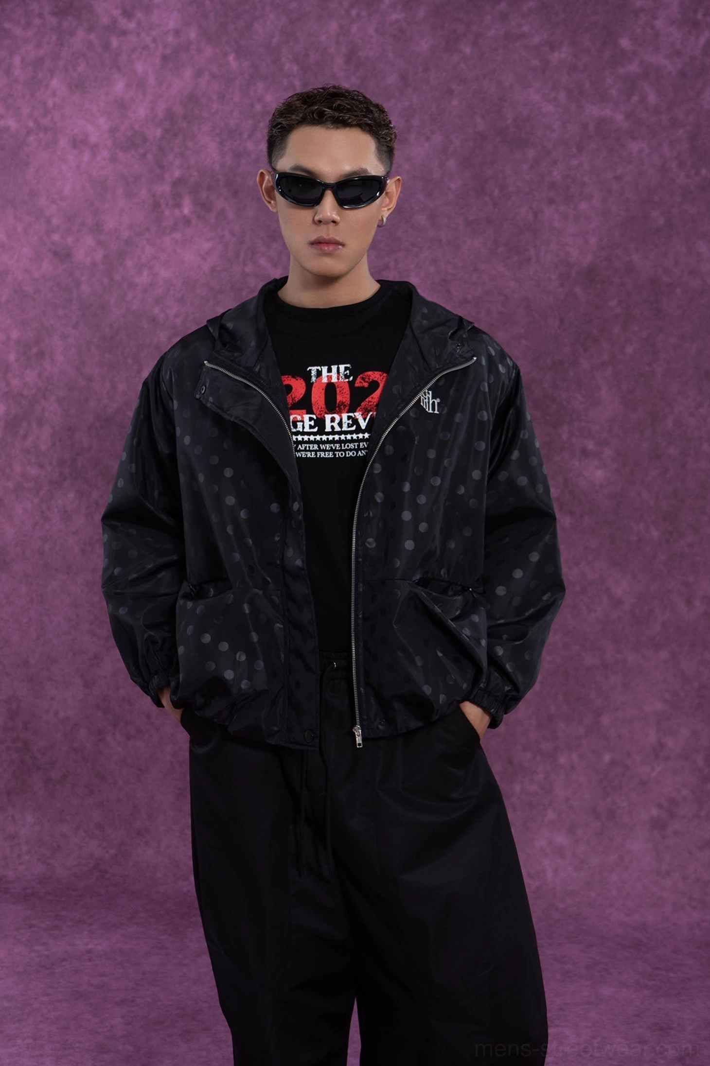 Black polka dot hooded windbreaker jacket worn open over a graphic tee in layered streetwear outfit