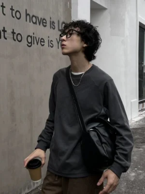 Black PU leather crossbody sling bag worn across the body by a male model holding coffee in an urban street setting