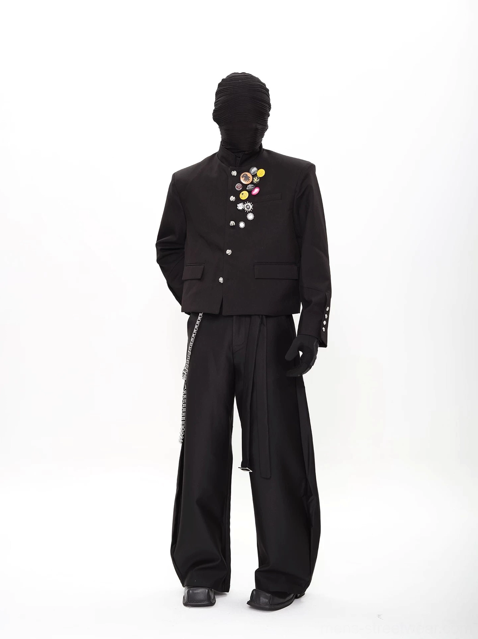 Left side view of black cropped punk blazer with chest badges paired with wide-leg suit pants and metal chain