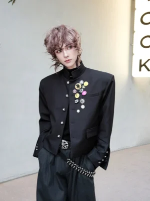 Black punk stand collar cropped bolero blazer worn by a male model outdoors, featuring silver buttons, chest enamel pins, and studded cuff hardware