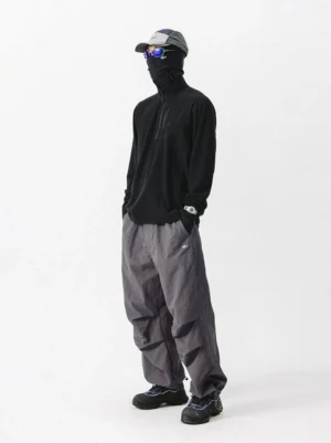 Black quarter zip fleece pullover side view with high collar styled with loose gray outdoor pants and neck gaiter