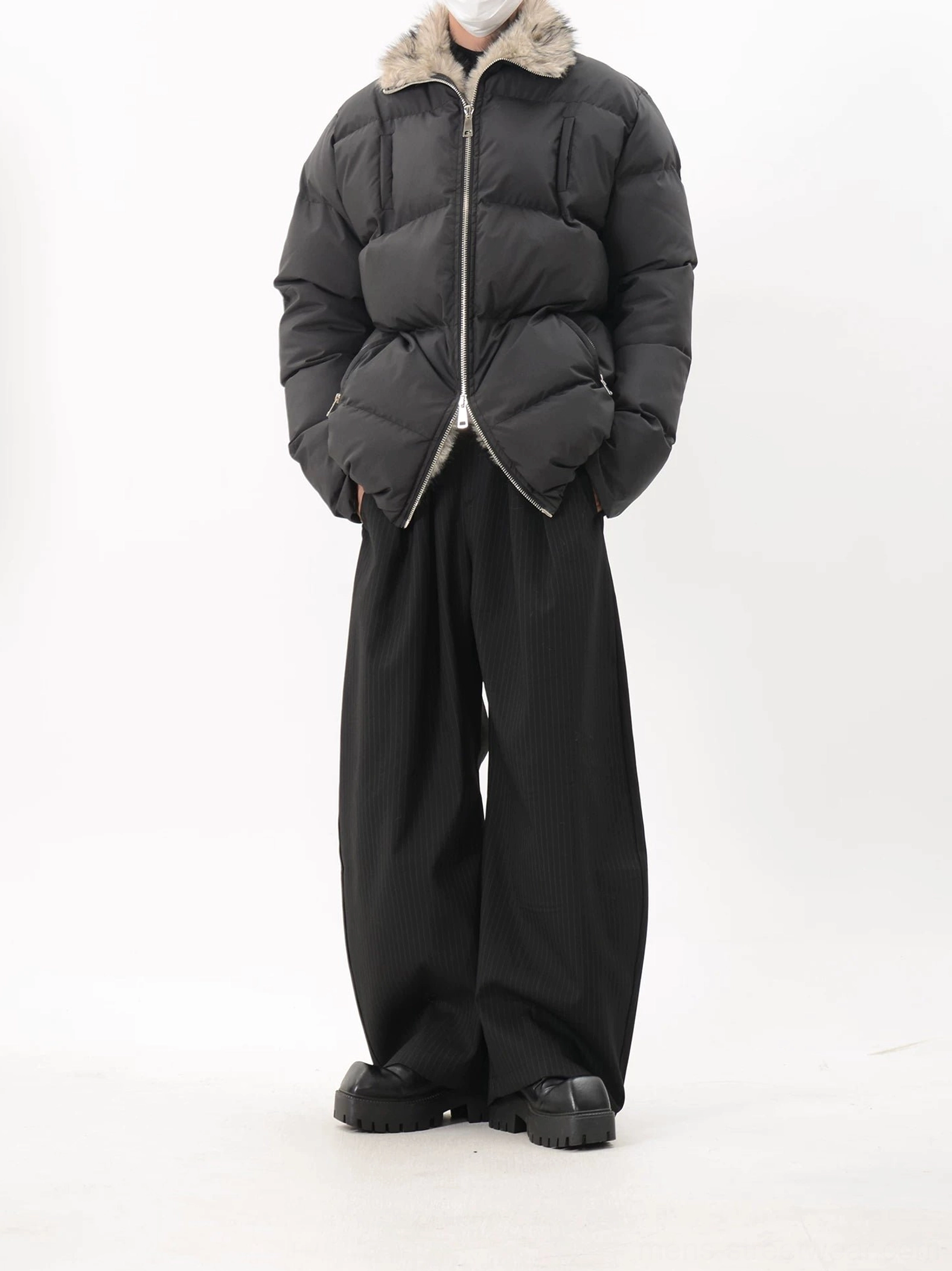 Full-body view of black oversized padded puffer jacket with fur-lined stand collar, wide-leg black pants, and chunky leather shoes